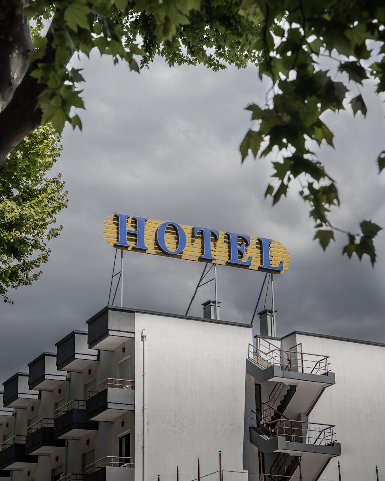 A modern hotel building with a prominent yellow sign against a cloudy sky, surrounded by greenery.