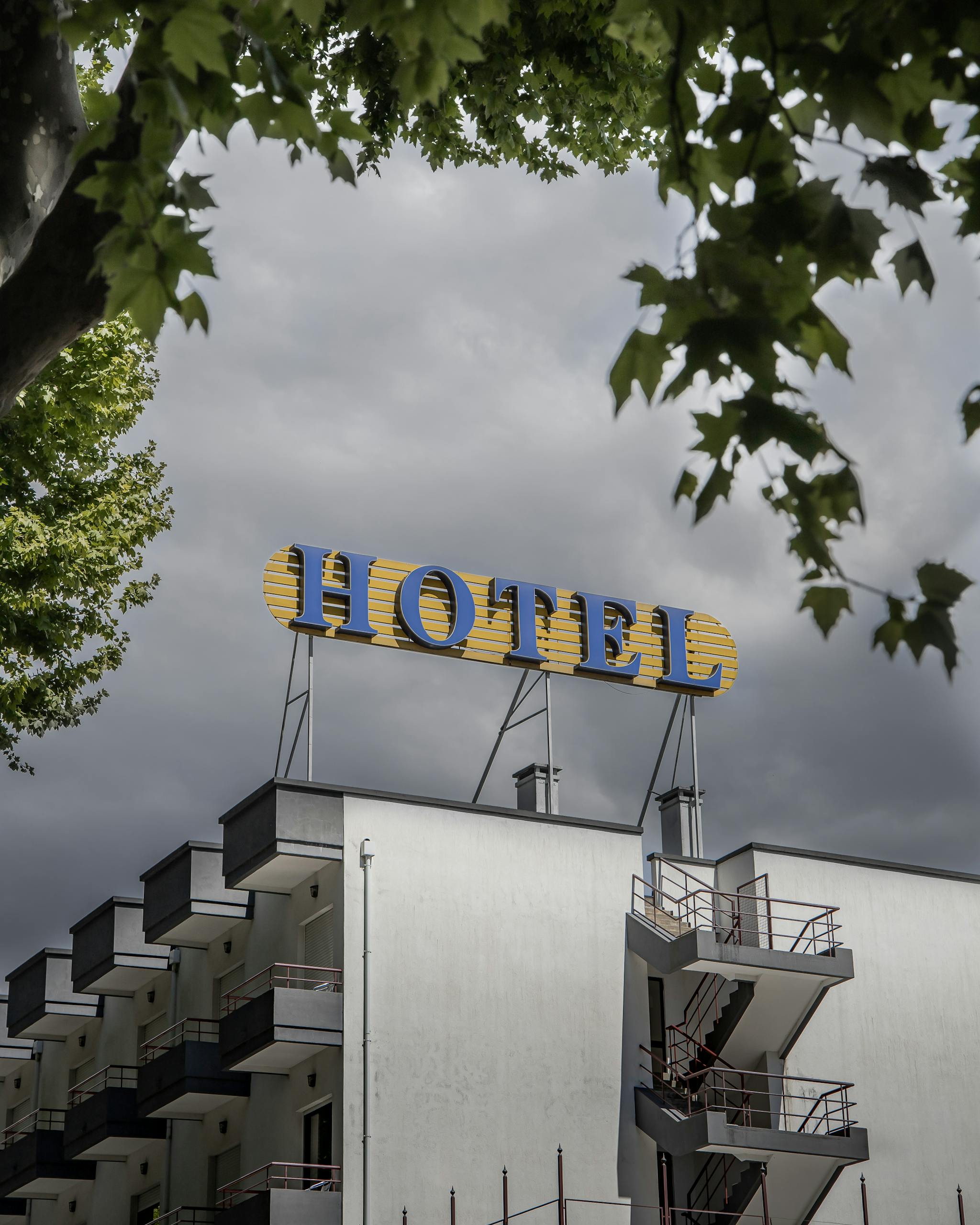 A modern hotel building with a prominent yellow sign against a cloudy sky, surrounded by greenery.