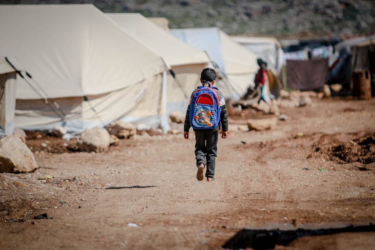 A young boy carrying a backpack walks in a refugee camp in Idlib, Syria.