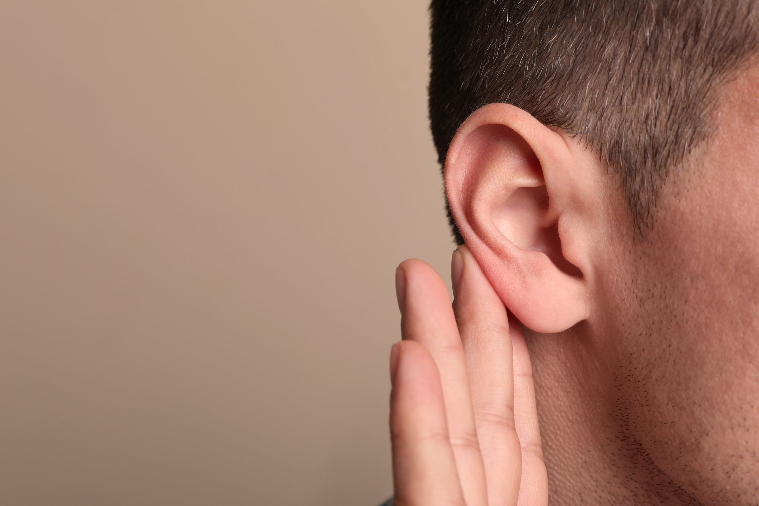 Man,Showing,Hand,To,Ear,Gesture,On,Beige,Background,,Closeup.